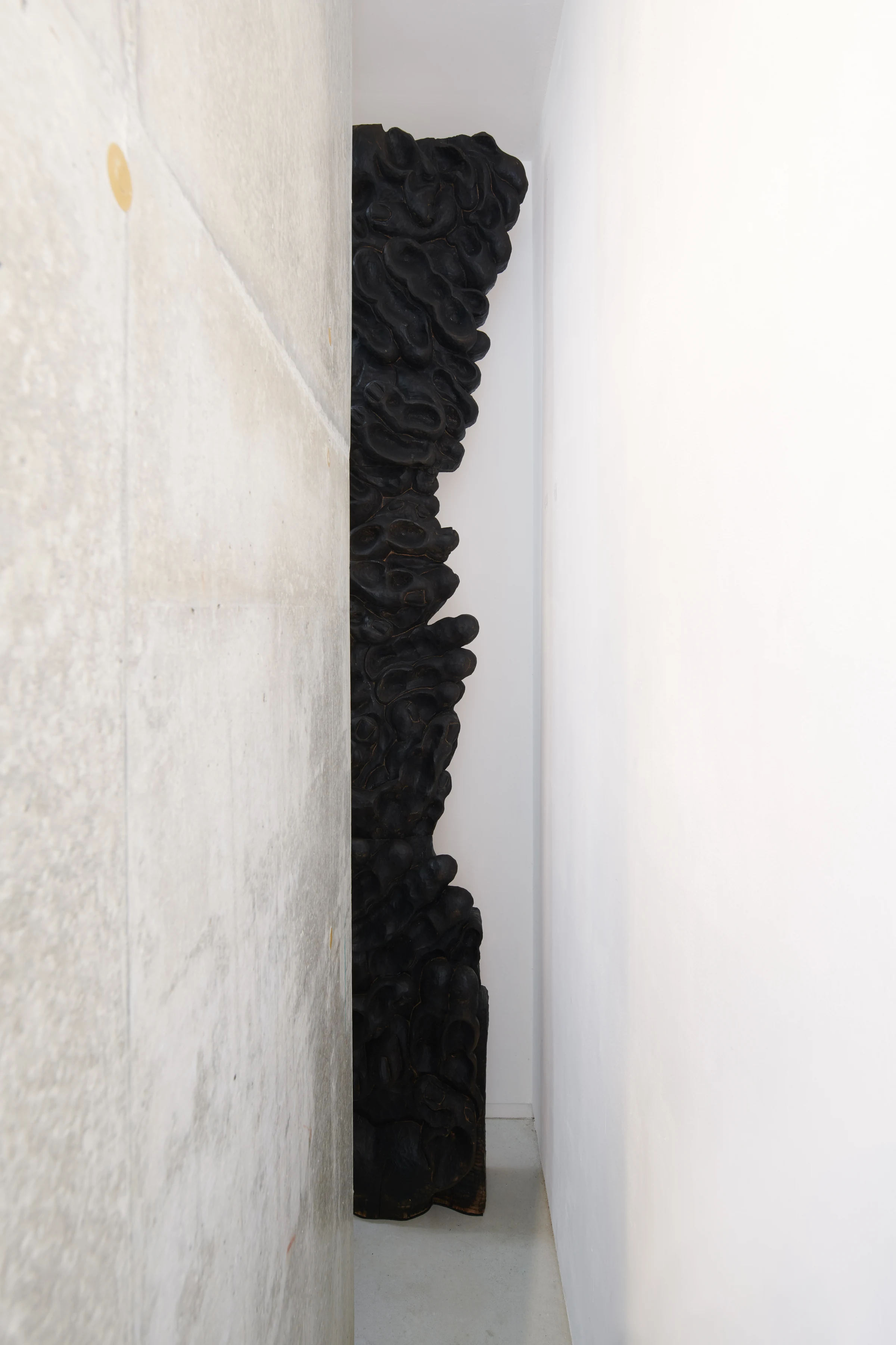 CAVE, a tall dark sculpture with hand-shaped impressions in a narrow space between walls