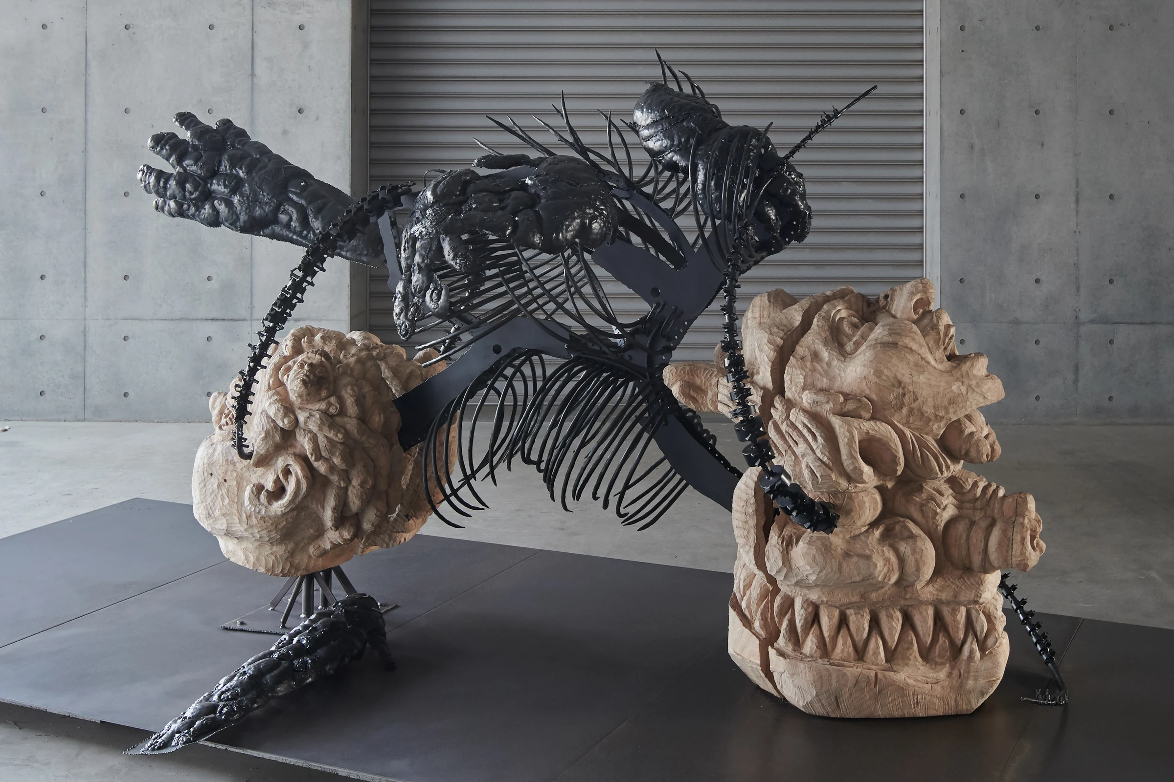 Nezha’s Bike, a sculpture with a dark skeletal framework and two large carved heads
