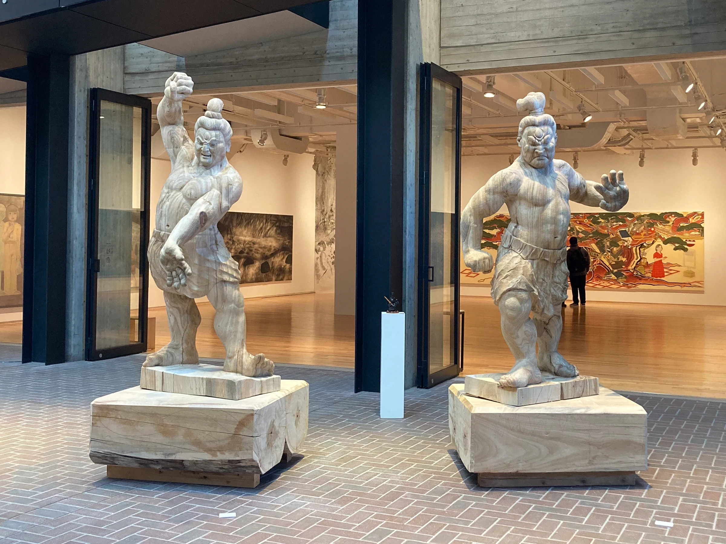 NIOU, two standing guardian figures on plinths at a gallery entrance